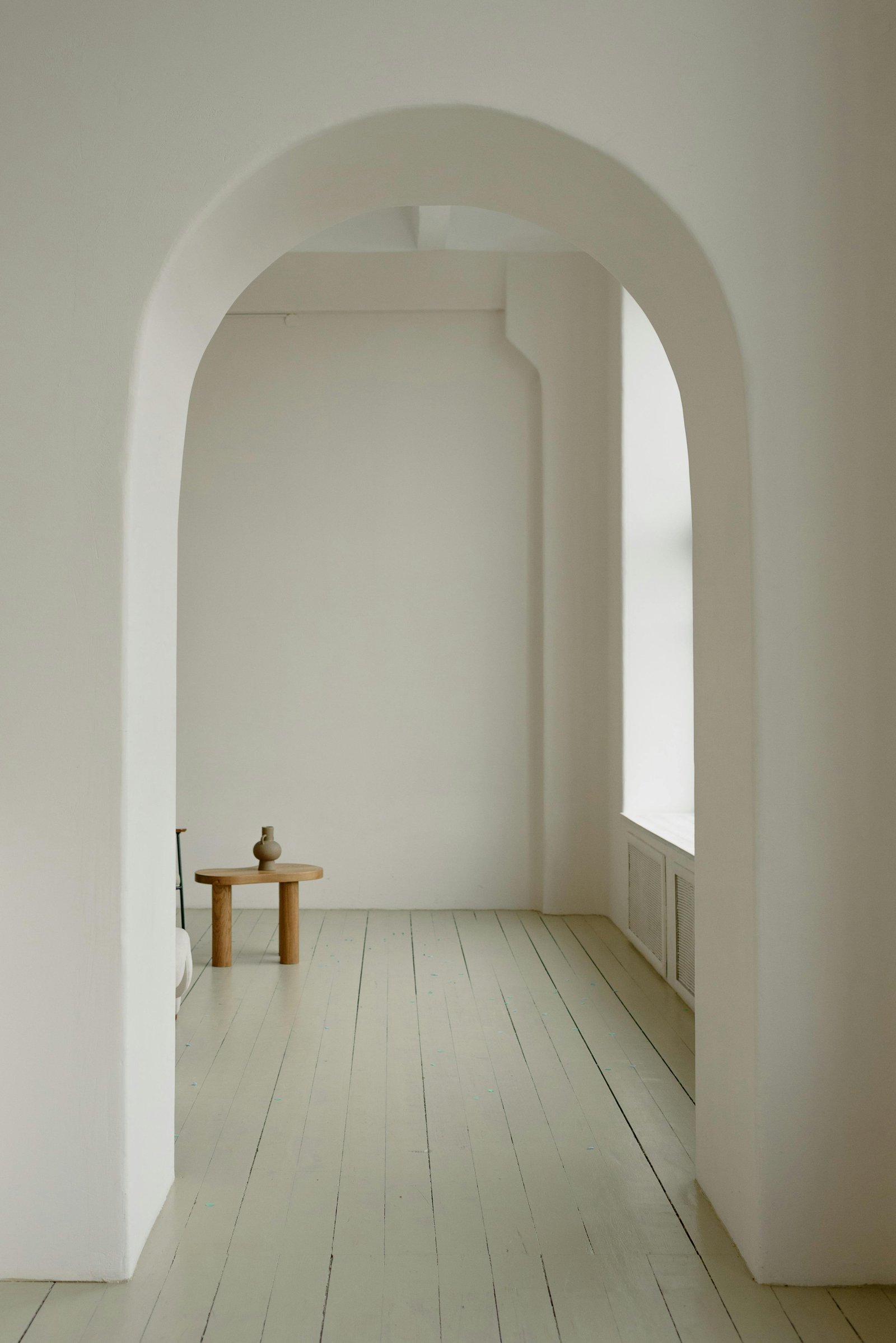 White lime-plaster arched threshold opening onto a sunlit room with a single wooden table — MarkOn® Walls atelier, by Vlad Markov